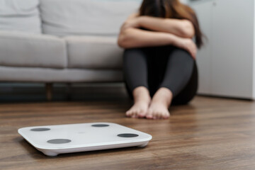 Fototapeta premium Sad woman with fat upset bored of dieting Weight loss fail&nbsp; Fat diet and scale sad asian woman on weight scale at home weight control