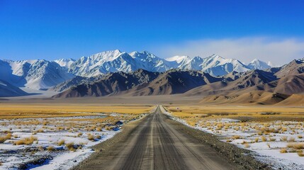 A wide road leads to the snow-capped mountains of Almaty. In the foreground, there is an endless desert with yellow grass and sand dunes, under a clear blue sky. 