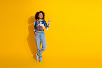 Happy young woman in casual outfit pointing up with cheerful expression standing against bright...