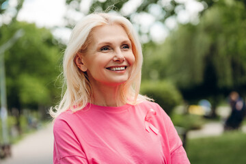 Senior woman smiling and showing pink ribbon for breast cancer awareness in park