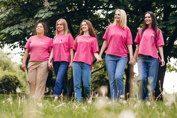 Women holding hands and wearing pink ribbons are walking in park for breast cancer awareness