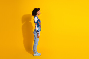 Side profile of a young woman with curly hair in casual wear, posing against a vibrant yellow...