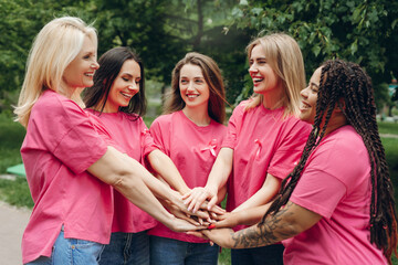 Fototapeta na wymiar Volunteers joining hands wearing pink ribbon for breast cancer awareness