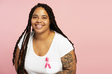 Young woman smiling and showing pink ribbon for breast cancer awareness