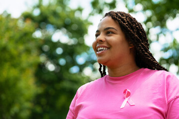 Young woman wearing pink ribbon is smiling in a park during a breast cancer awareness event