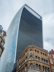 Walkie Talkie building in London, tall skyscraper seen from below with cloudy sky background. Contrast between old architecture and modern glass structure with Sky garden above