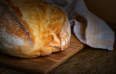 Freshly baked rustic bread resting on a wooden cutting board next to a linen cloth in a cozy kitchen setting
