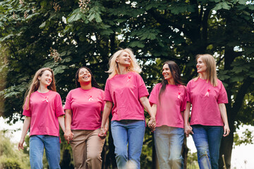 Smiling multinational women wearing pink ribbons for breast cancer awareness walking in park