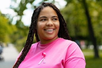 Young African American woman smiling and showing pink ribbon for breast cancer awareness