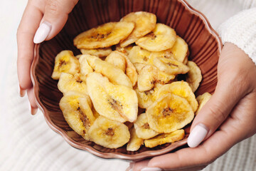 Tasty banana chips in bowl. Healthy fruit snack served in hands. Crispy golden slices of dried banana. Natural sweet treat for diet and energy. Vegan food with tropical flavor and crunchy texture.