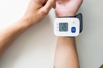 Man using digital wrist blood pressure monitor for measuring blood pressure and pulse. Managing...