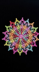 A colorful, intricate, symmetrical, handmade doily pattern against black background.