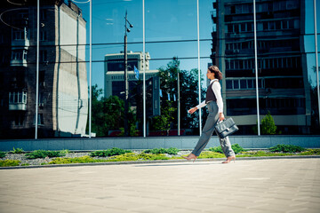 Obraz premium Businesswoman Walking Outside a Modern Urban Office Building Holding a Briefcase on a Bright Sunny Day