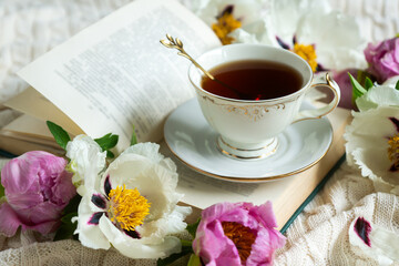Peony flowers and a cup of tea, books on a white blanket.