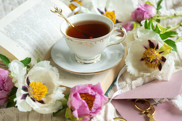 Peony flowers and a cup of tea, books on a white blanket.