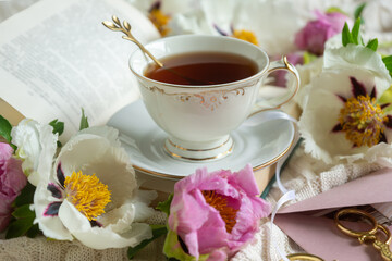 Peony flowers and a cup of tea, books on a white blanket.