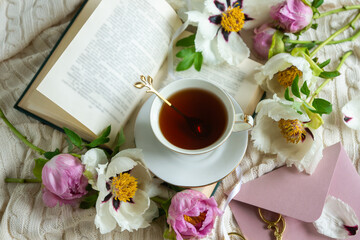 Peony flowers and a cup of tea, books on a white blanket.
