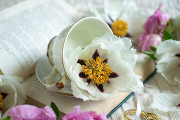 Peony flowers and a cup of tea, books on a white blanket.