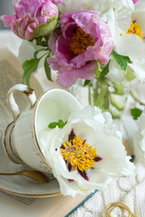Peony flowers and a cup of tea, books on a white blanket.