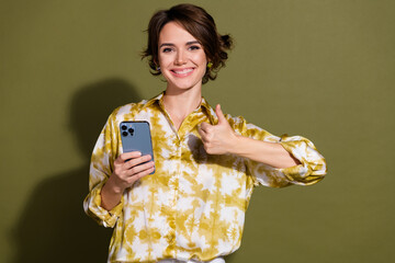 Confident young businesswoman giving a thumbs up in stylish blouse against khaki background