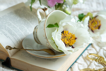 Peony flowers and a cup of tea, books on a white blanket.