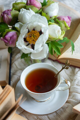 Peony flowers and a cup of tea, books on a white blanket.