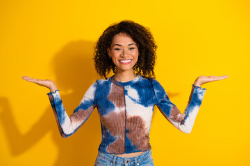 Stylish young woman with curly hair in brightly colored attire posing confidently against a solid...