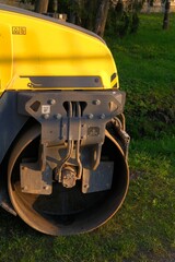 Yellow construction roller drum machine parked on green grass. Construction and landscaping vehicle and equipment. Compaction tasks during earthwork, landfills and agriculture maintenance