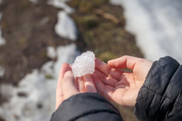 
hands holding a piece of snow or ice, with a blurred snowy ground in the background.