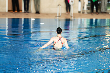 Solo female swimmer performing artistic moves in a pool during a public aquatic event, showcasing...