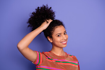Cheerful young woman with curly hair smiling against a purple background showcasing vibrant fashion...