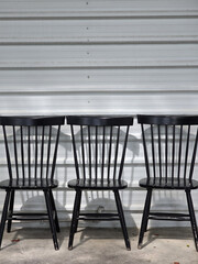 Black wooden chairs arranged against metal wall, showcasing their sleek design and shadows. simplicity of chairs adds modern touch to industrial setting