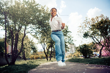 Young woman enjoying a sunny day outdoors in a city park, jumping happily surrounded by greenery...