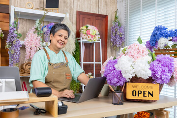 Asian senior woman, florist, small business, owner, entrepreneur manage store accounting with laptop at flower shop, independent lifestyle, creative workspace, passion for business, and modern skills