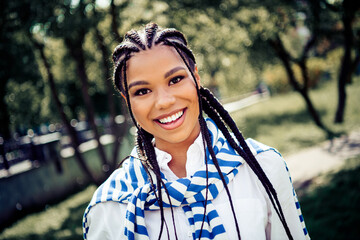 Cute beautiful woman with braided hair smiling brightly in a sunny urban park with lush greenery...