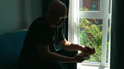 Retired senior man counting pension cash. Elderly male managing retirement money by window. Older person holding UK banknotes indoors. Pensioner handling ten pound notes in daylight
