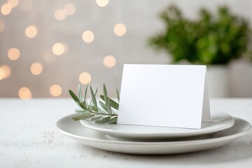 Elegant blank card placed on a white plate with fresh olive branch, surrounded by soft bokeh lights, creating a serene atmosphere perfect for invitations or special occasions with copy space