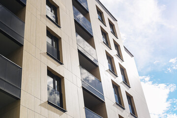 Modern apartment building facade. Residential architecture with balconies and large windows. Urban housing complex under blue sky. Minimalist exterior with beige and black wall materials.