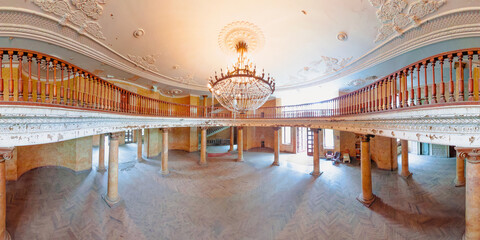 Wide angle view of decaying ballroom with wooden balustrade and columns supporting a balcony, under...
