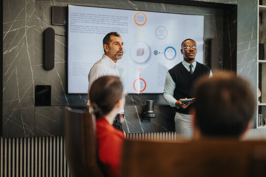 A diverse group of people gathered in a modern conference room, actively discussing business strategies and presentations. The atmosphere is dynamic and focused, emphasizing teamwork and collaboration