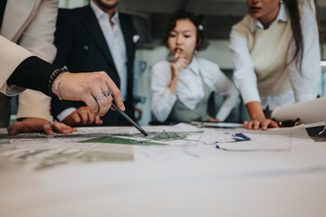 Naklejka na ściany i meble A group of diverse people gather around a table, analyzing blueprints. The project leader uses crutches while guiding the team's discussion on the project details.