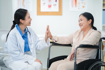 Asian female doctor giving a cheerful high five to an elderly woman patient, both smiling warmly in a medical clinic setting. A joyful moment of healthcare connection, trust, and support between careg