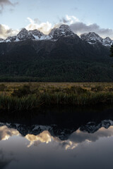 Snow-capped peaks loom above a dense forest, mirrored with stunning clarity in the still waters...