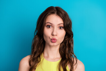 Young woman in a yellow dress making a funny face against a bright blue background expressing...