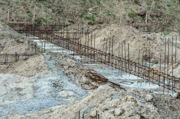 Construction site with bare earth and gravel shows rebar framework positioned for foundation,...