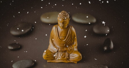 Displaying wooden meditating statue sitting on tabletop with river stones and white star overlays