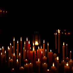 Many burning paraffin candles and glowing lamp in dark room