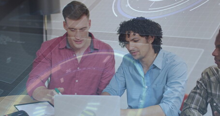 Collaborating coworkers wearing shirts and working on laptop at office table with notebook pen