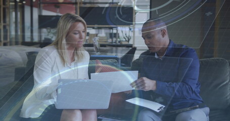 Business casual colleagues in office lounge collaborating on printed documents, with laptop