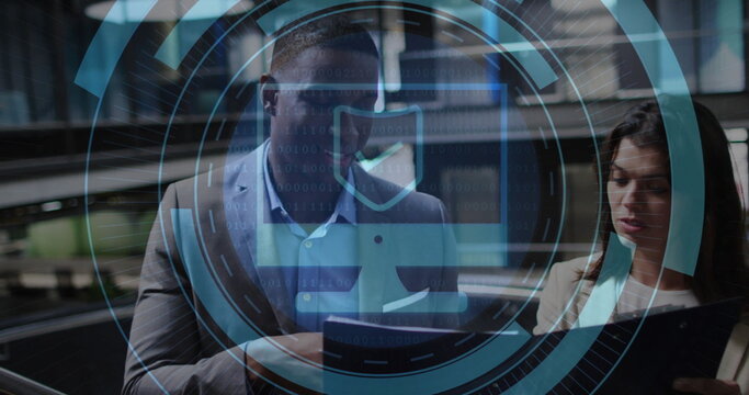 Reviewing tablet and printouts by team in business attire in office hallway, cybersecurity overlay